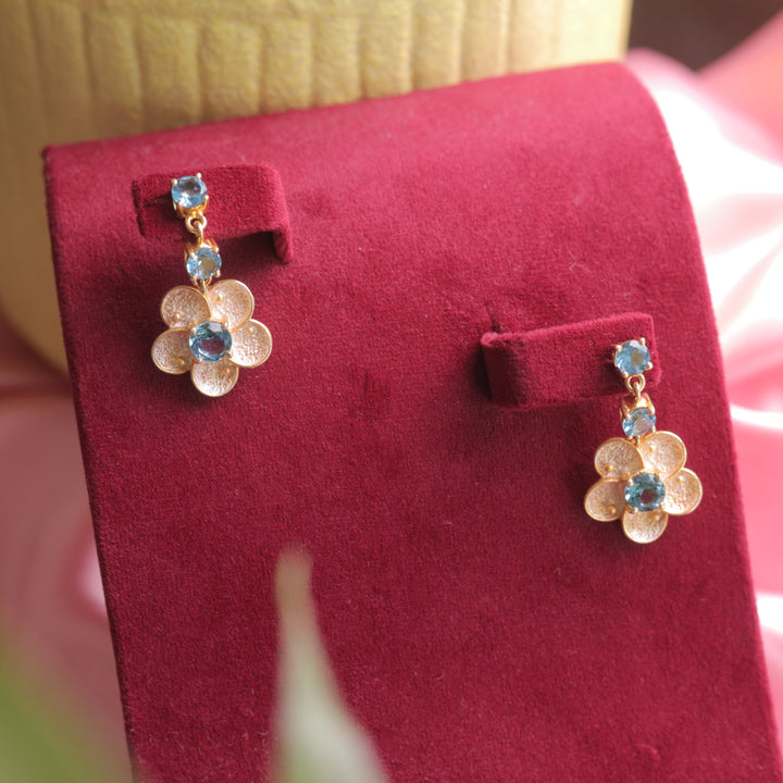 A close-up of London Blue Topaz Floral Earrings, featuring a deep blue gemstone.
